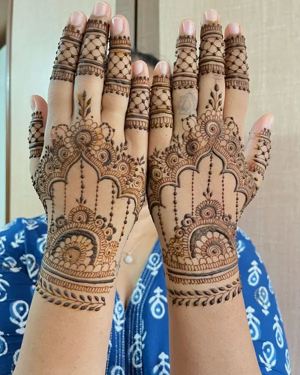 A beautiful semi bridal mehndi design for a wedding guest, featuring matching intricate patterns on both hands. The design includes detailed archways, hanging elements, and leafy wrist cuffs.