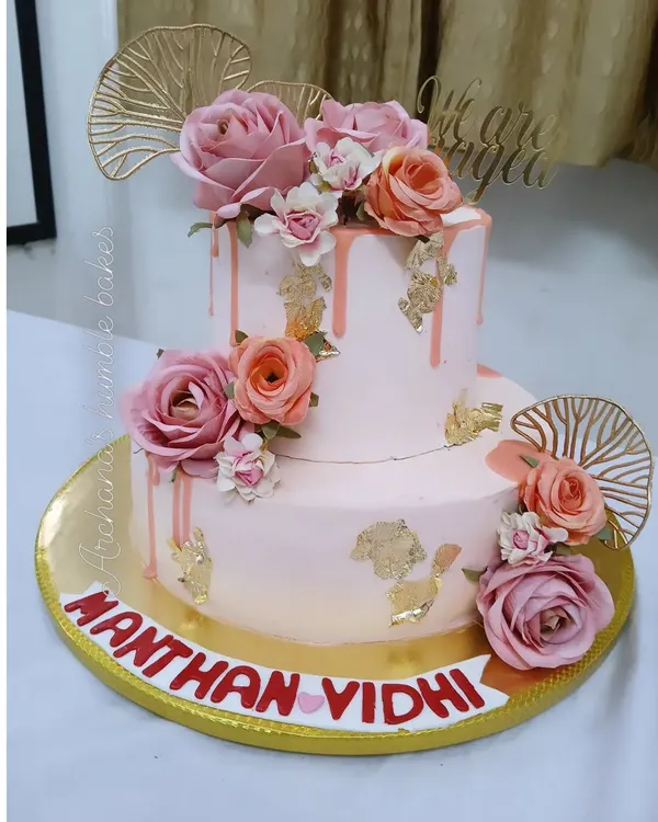 A stunning two-tiered engagement cake in soft pink, adorned with fresh roses, gold leaf, and a drip effect. I love creating these romantic centerpieces.
