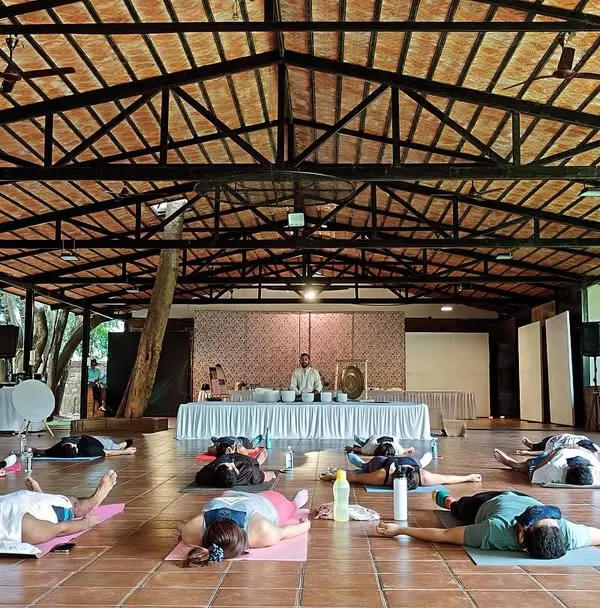 A large group experiences deep rest during a sound meditation workshop in a beautiful, open-air hall. This setting allows participants to connect with both the healing sounds and the tranquility of nature.
