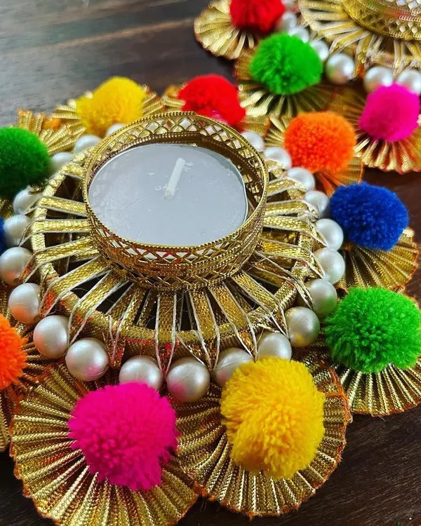 We are all about adding that festive vibe to your home. This is a close-up of our handmade tea light holder, decorated with gota patti, bright pompoms, and delicate pearls, perfect for your Diwali decor.
