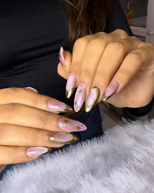 An elegant and celestial-inspired design featuring long extensions with a sheer pink base, gold chrome tips, and delicate gold starburst details.