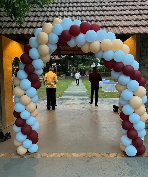 A beautiful organic balloon arch in muted tones of maroon, beige, and light blue, creating an elegant entrance for an outdoor event.