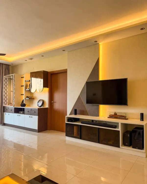 A beautifully lit living room featuring warm cove lighting above the TV unit and accent lights in the shelving. The entire setup is automated for mood control.