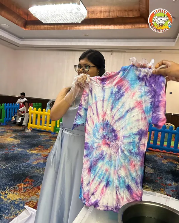 The big reveal. A student proudly displays her finished tie-dye T-shirt, a vibrant explosion of color created during one of our corporate event workshops.