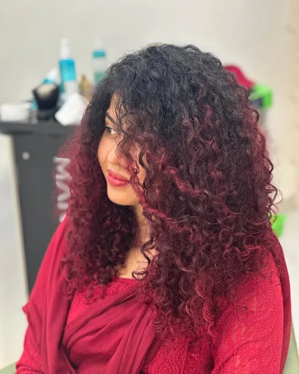 A full view of this stunning red balayage on long, beautiful curls. The color is strategically placed to create dimension and movement, making the curls pop. This shows how vibrant color can work in harmony with natural texture.