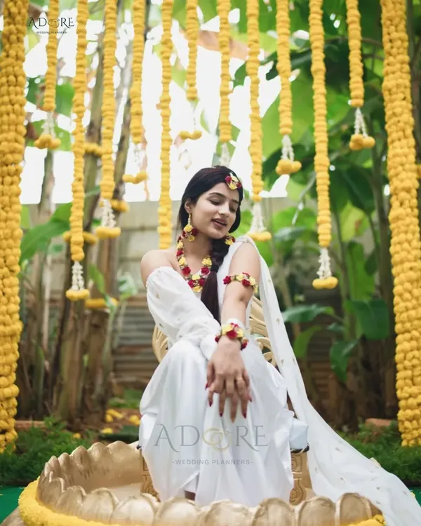 A beautiful bride enjoying her Haldi ceremony. The backdrop of hanging yellow chrysanthemums and lush greenery creates a vibrant and joyful atmosphere, perfect for this pre-wedding ritual.