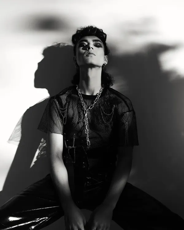 A dramatic, high-contrast black and white portrait from a punk-inspired men's editorial. The play of harsh light and deep shadow creates a powerful, graphic image.
