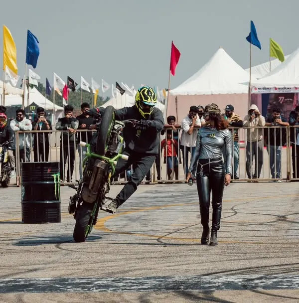 A professional stunt rider performs a wheelie in the stunt zone, surrounded by an engaged crowd and Monster Energy branding. This is brand activation at its most exciting.