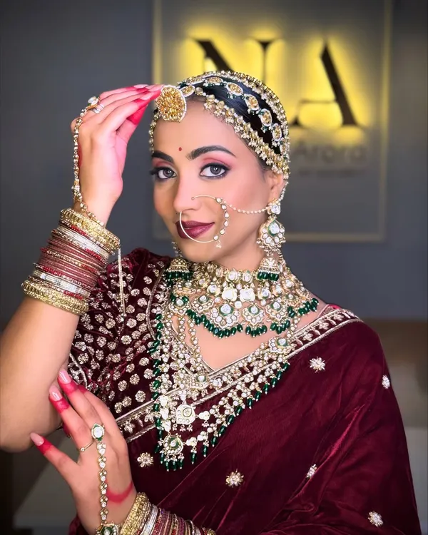 A royal Marwadi bride in a deep velvet lehenga. The look features dramatic eyes, bold red nails, and intricate jewelry, including a traditional sheeshpatti, to create a timeless and elegant style.
