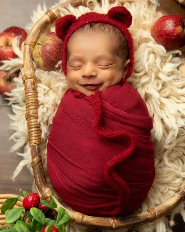 This little smile is everything. I focus on capturing these fleeting, precious moments of pure joy. This is a classic swaddled pose in a cozy basket, using a vibrant red wrap that makes the photo feel so warm and full of love.