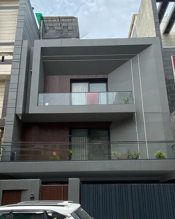 The completed facade of the Delhi residence, shown as a 3D render in image 18. This real-world photo confirms the faithful execution of the design's core elements, from the recessed wooden paneling to the prominent grey frame of the upper balcony.