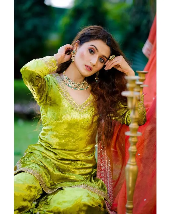 A vibrant outdoor portrait of a model in a lime green velvet suit, accessorized with a statement necklace. The natural lighting beautifully captures the fabric's sheen and the jewelry's detail for a fashion campaign.