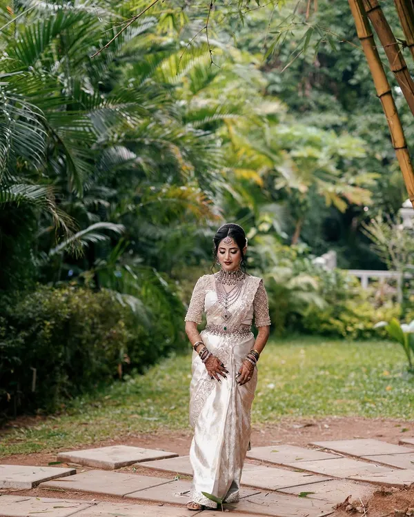 A full-length shot of the beautiful Dr. Ankita, showcasing how the intricate mehendi on her hands and feet complements her stunning white and silver saree and traditional jewelry.