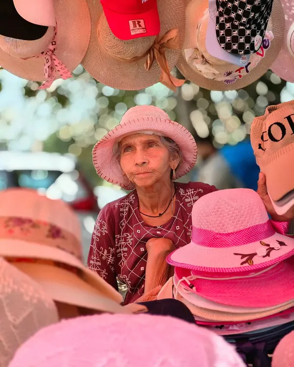 A candid portrait of an elderly woman selling hats at a market in Goa. Her expressive face tells a story of a life lived by the sea, captured using my OPPO phone's portrait mode.