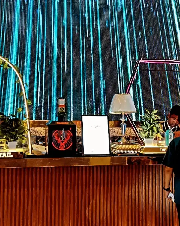 A sleek, modern bar with a wooden finish set against a massive digital LED screen, creating a dynamic and high-tech backdrop for a wedding cocktail event.