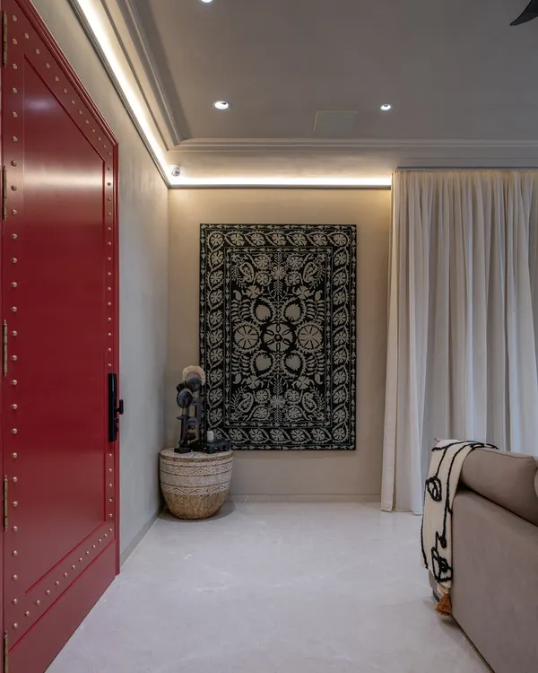 A bold, brass-detailed red door makes a powerful statement in this living room. I contrasted it with a hand-embroidered wall panel and lime-plastered walls, layering global artifacts to create a contemporary space that is both warm and culturally rich.