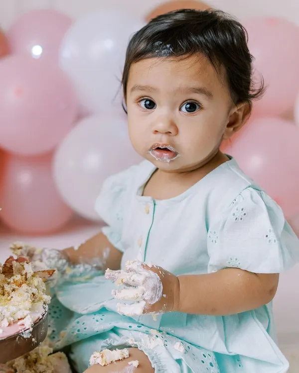 The pure joy of a first birthday cake smash. This little girl is having the best time, and her happy, messy face says it all.