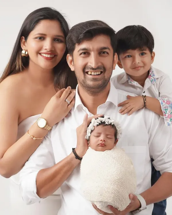 A classic family portrait against a clean white background, featuring parents and their two children, including a swaddled newborn held by the father.