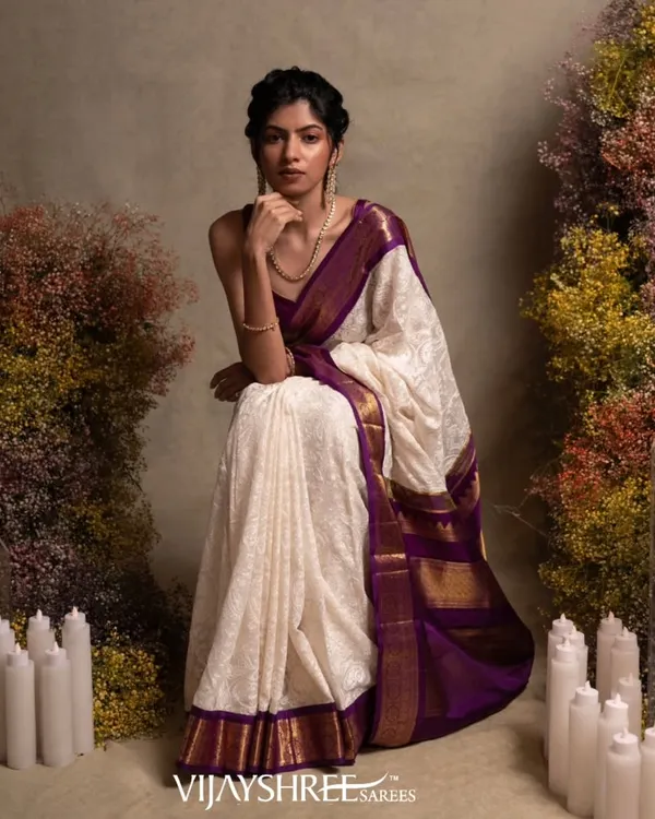 A masterpiece of fusion, this white Kanjivaram saree is adorned with exquisite Chikankari hand embroidery, set against a rich purple border and pallu.
