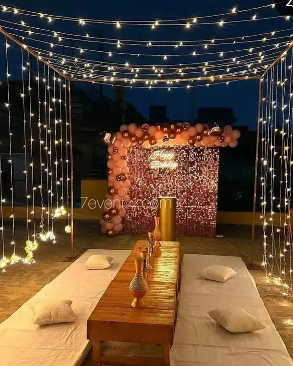 A beautiful terrace dining setup perfect for a romantic evening. This arrangement features a canopy of fairy lights, low seating with comfortable cushions, and a decorated backdrop, creating a private and magical atmosphere under the stars.
