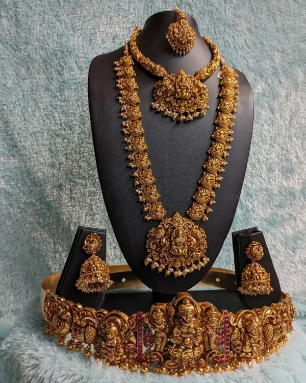 This is the quintessential full bridal temple jewellery set for a traditional South Indian wedding. It includes a choker, a long Laxmi haaram, matching jhumkas, and an intricate hip belt (vaddanam), all in a beautiful antique gold finish.