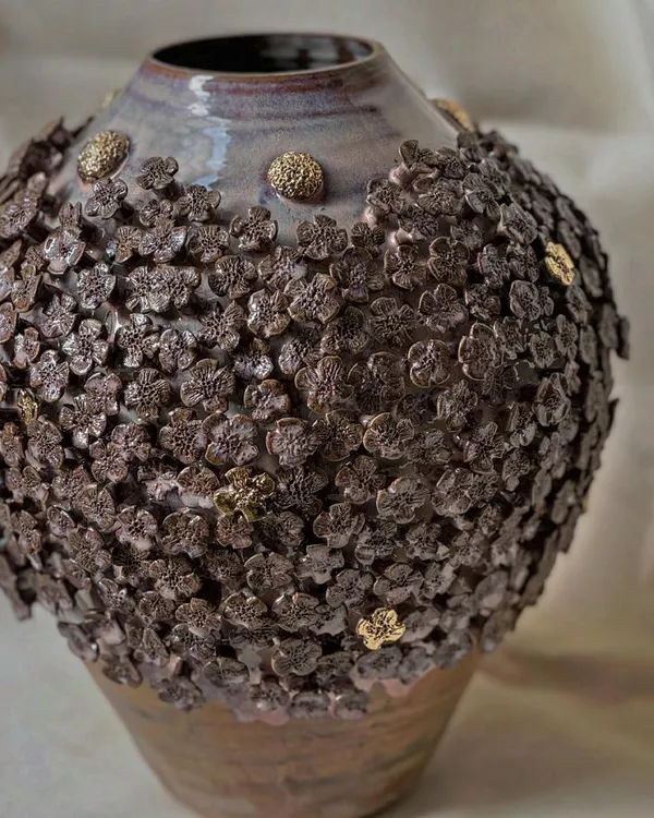 A close-up of the 'Floral Grace' vase, showing the texture and detail of the hand-applied stoneware flowers with gold accents. Each flower is attached one by one, making every vase truly unique.