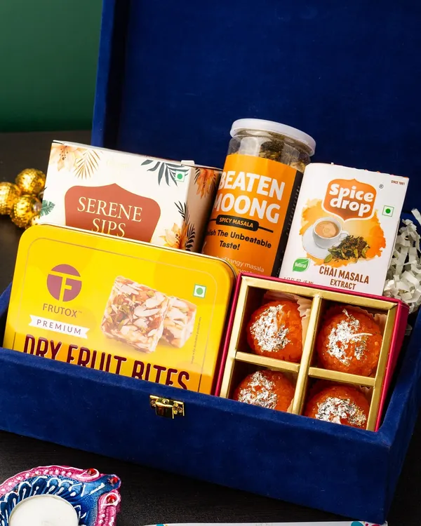 This luxurious royal blue velvet box is curated for a premium gifting experience. It contains a mix of healthy snacks like dry fruit bites and beaten moong, gourmet tea, and traditional motichoor ladoos, making it a perfect blend of health and indulgence for Diwali.