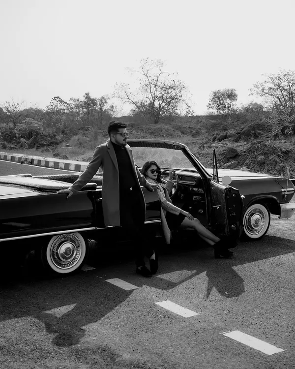 A classic black and white shot from a vintage-themed pre-wedding shoot. The convertible car and the couple's stylish outfits create a timeless, cinematic feel that is both cool and romantic.