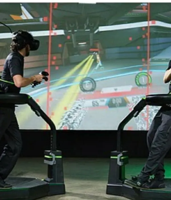 Two players work together in a multiplayer game on the Virtuix Omni treadmills. This setup encourages communication and strategy, making it an effective and exciting tool for corporate team-building workshops.