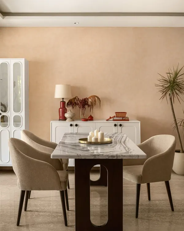 I believe a dining room should be the heart of the home, a place that naturally draws people together. Here, the warm, earthy tones on the walls and the elegant marble tabletop create an inviting atmosphere for shared meals and conversations. The space is completed with a simple white crockery unit and touches of red and brass, making it feel cherished and lived-in.
