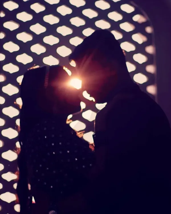 A beautiful silhouette of a couple with the sun flaring between them, framed by an intricate jaali window.