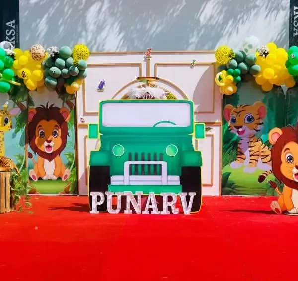 A full view of a jungle-themed birthday party setup. I used a large jeep cutout as the centerpiece, surrounded by cute animal characters, balloon garlands, and a personalized name sign for Punarv.