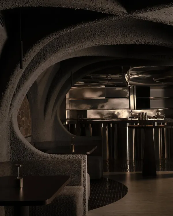 The entrance to the dining area, where the dialogue between rough concrete and polished steel begins. The curved forms guide the eye and body, creating an organic flow through a space that feels discovered, not just entered.