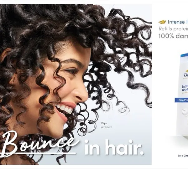 A dynamic advertisement for Dove's 'Intense Repair' range. The shot captures the joyful bounce of a model's curly hair, visually representing the campaign tagline "Fill Bounce in hair" alongside the product packshot.