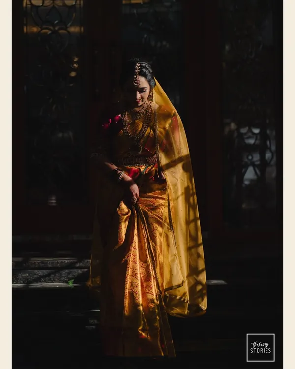 A breathtaking bridal portrait using dramatic lighting to create a powerful and artistic image. The bride, draped in a golden saree, looks like a timeless painting.