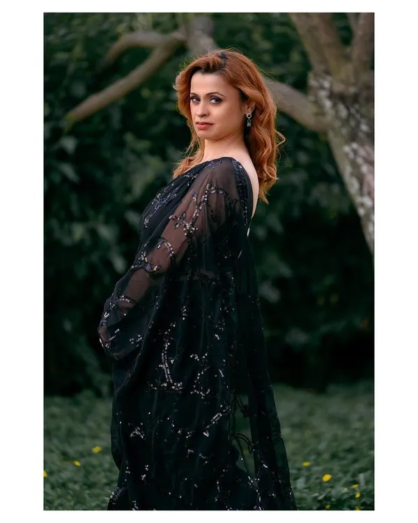 An elegant outdoor portrait of a woman in a beautiful black saree. The natural green background provides a perfect contrast, making the subject stand out.