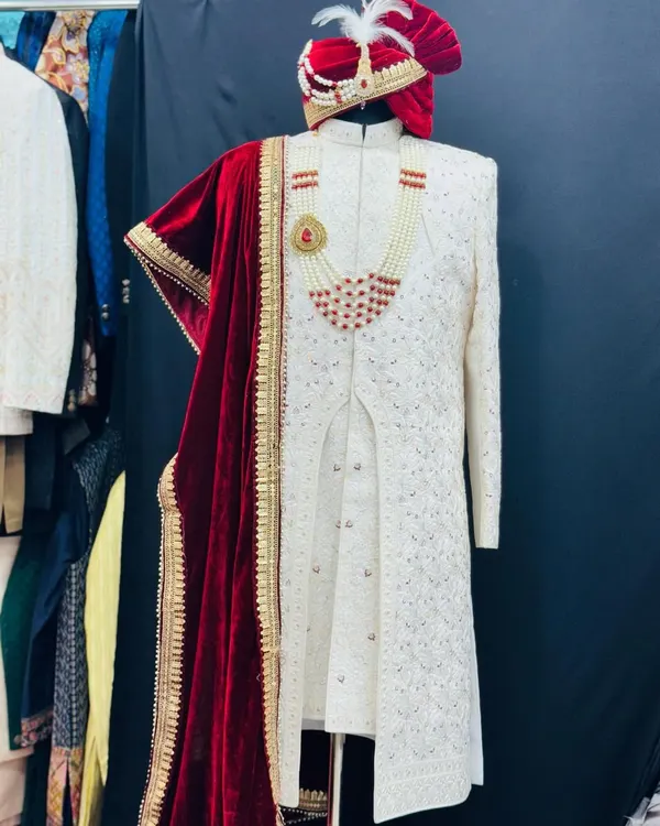 A full view of a trending floral hand-detailed sherwani. This ivory piece is paired with a rich red velvet dupatta, a custom turban, and a pearl necklace, creating a complete and majestic groom's ensemble.