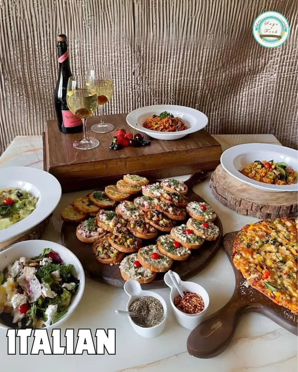 An elegant Italian spread perfect for a celebration. This image features a large bruschetta platter, artisanal pizza, fresh salads, and pasta, paired with sparkling wine for a complete dining experience.