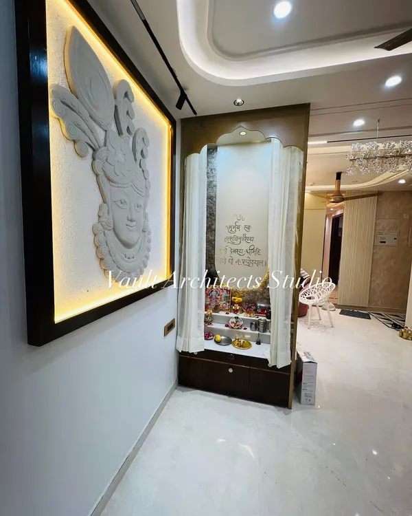 The final look of a serene pooja corner. This space features a custom-made temple with delicate curtains and a stunning, backlit Krishna stone mural on the adjacent wall.