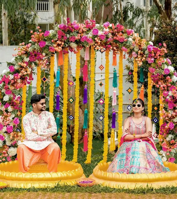 A cool and quirky Haldi portrait, with the couple wearing sunglasses against a stunning floral and tassel backdrop.