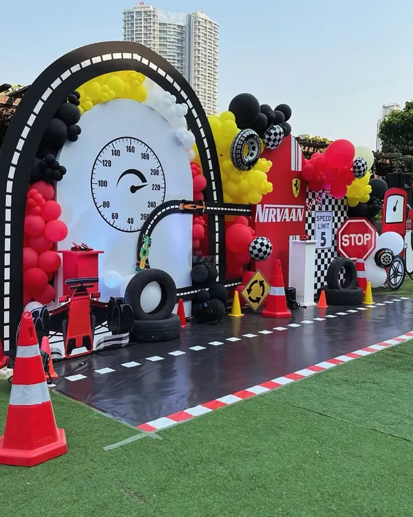 Ready, set, go! A full-throttle race car party setup with a custom track, a speedometer backdrop, and tons of themed props like tires, traffic cones, and a fuel station.