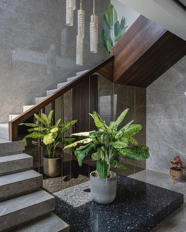 This staircase in the 'Aria Residence' is a centerpiece of the home. We used grey marble for the steps and a rich veneer for the underside and railing, creating a beautiful contrast. The space underneath is utilized for greenery, bringing nature indoors.