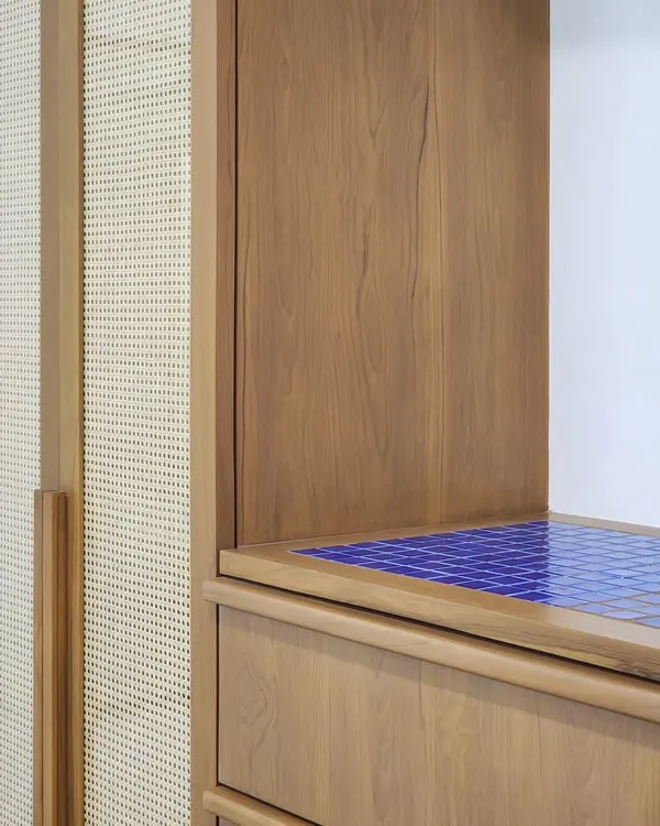 A detail showing the junction of materials in a custom furniture piece. The warmth of the wood and cane is punctuated by a surprising pop of vibrant blue tile, creating a unique and playful accent.