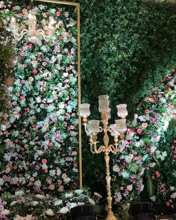 A close-up of a lush floral wall, showing the rich texture created by mixing different types of flowers and greenery, accented by an elegant candelabra.