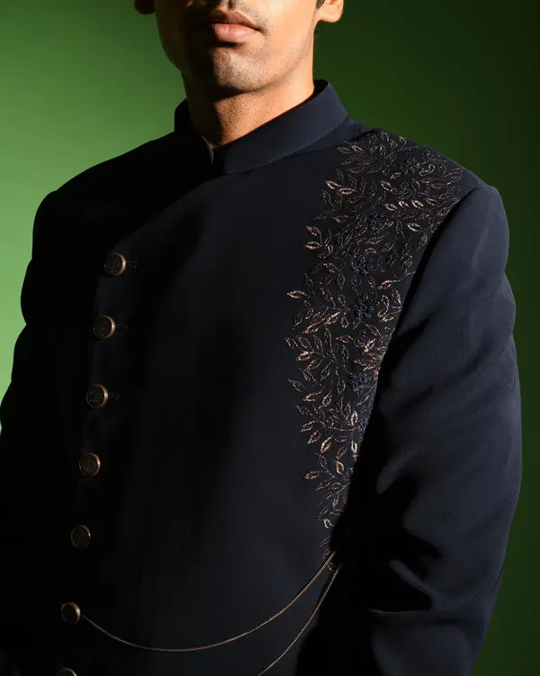 A close up of the dark navy asymmetric jacket, focusing on the intricate leaf embroidery that cascades down one side. This detail adds a touch of organic artistry to the sharp, structured design of the jacket.