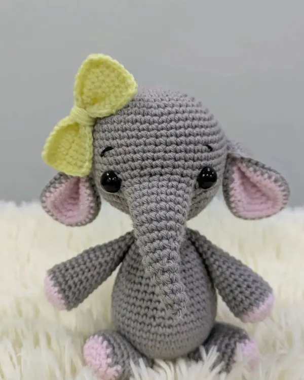 A very cute grey elephant with big ears, pink accents, and a sweet yellow bow on her head.