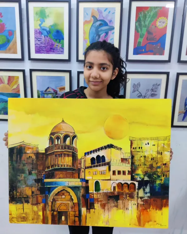 A student proudly displays her large-scale acrylic painting of a historic Indian city, bathed in a warm, golden light. This piece showcases advanced skills in architectural detail and color blending.