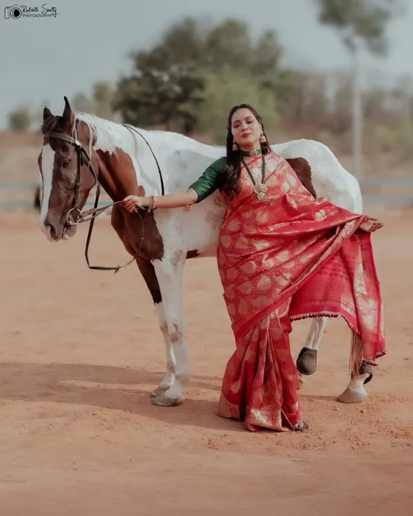 A beautiful and graceful shot from a conceptual shoot with a horse. The model's pose and the way she holds her saree create a sense of movement and elegance.