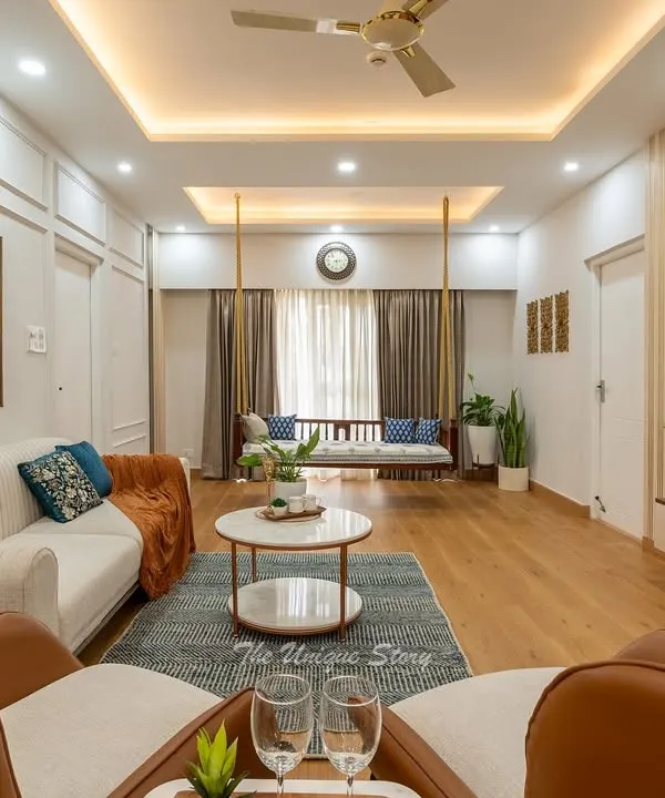 This expansive neo-classical living room is designed for effortless luxury and social gatherings. We combined a neutral palette with rich textures, including plush sofas, elegant armchairs, and warm wooden flooring, all illuminated by layered cove lighting to create an inviting ambiance. The traditional swing adds a touch of playful heritage to the modern setting.