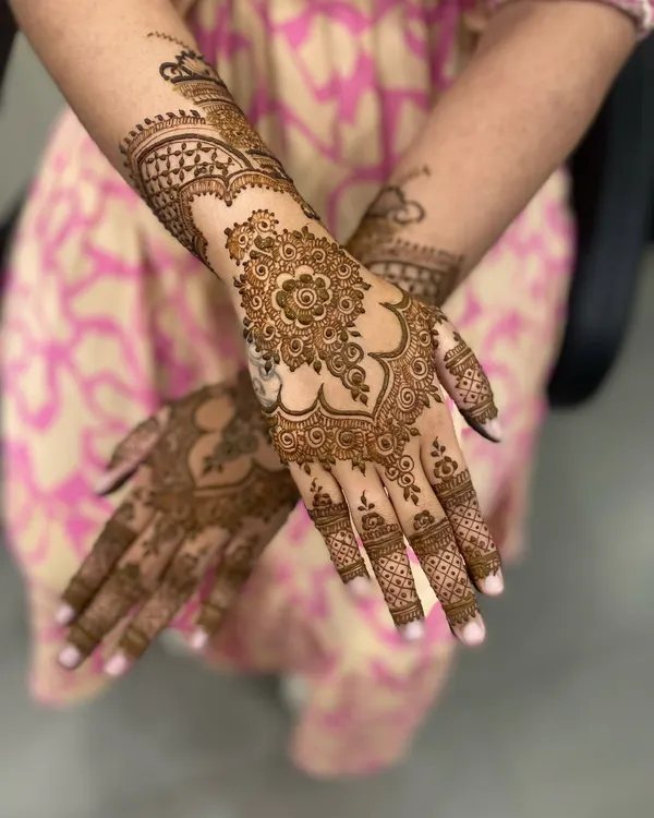 A classic Arabic mehandi design, featuring a bold floral mandala on the back of the hand with patterns extending to the fingers and arm.